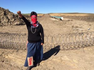 A masked warrior woman raises her fist at a Dakota Access construction site./Photo by Doug Grandt